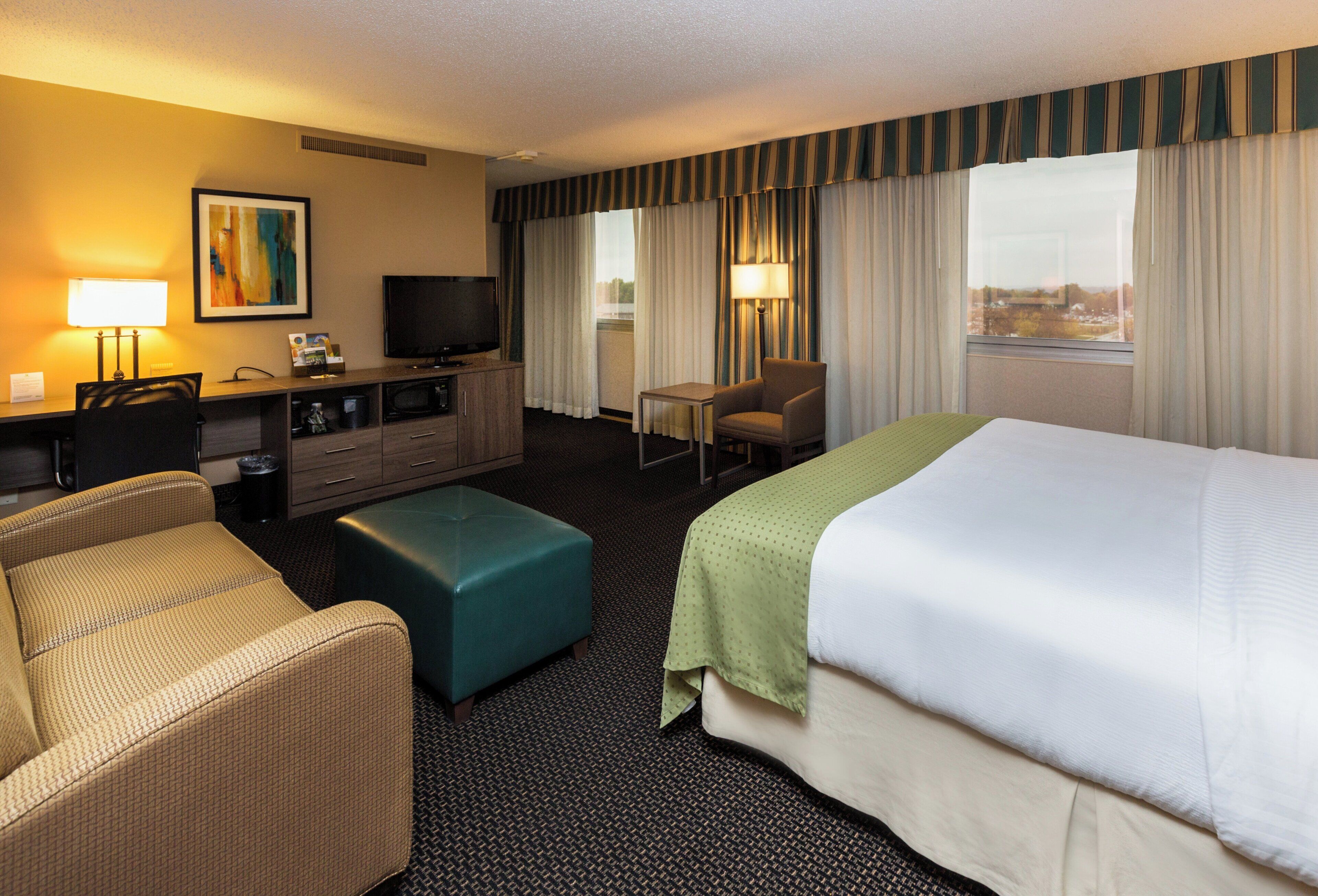 A hotel room with a bed, a desk with a computer, a television, a chair, and a couch.