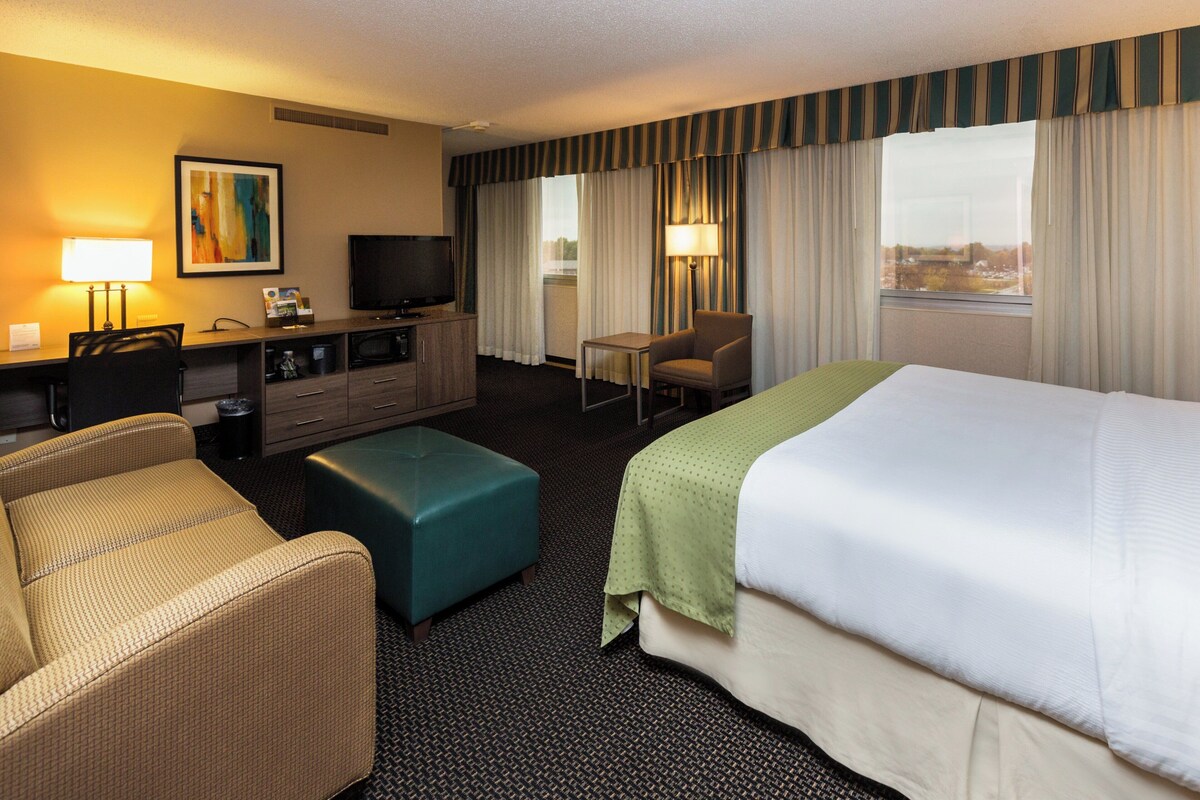 Ein Hotelzimmer mit Bett, Schreibtisch mit Computer, Fernseher, Sessel und einer Couch.