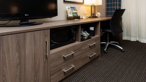 A hotel room with a flat-screen TV, a desk with a lamp, a microwave, and a chair. - Holiday Inn Downtown - Mercy Area by IHG (Des Moines)