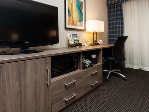 Ein Hotelzimmer mit Flachbildfernseher, Schreibtisch mit Lampe, Mikrowelle und einem Sessel.
