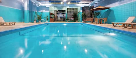 Una piscina interior con agua cristalina, rodeada de sillones de descanso y plantas en macetas.