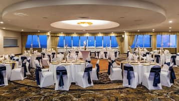 Un salón de banquetes con mesas redondas, manteles blancos y sillas con cintas azules.