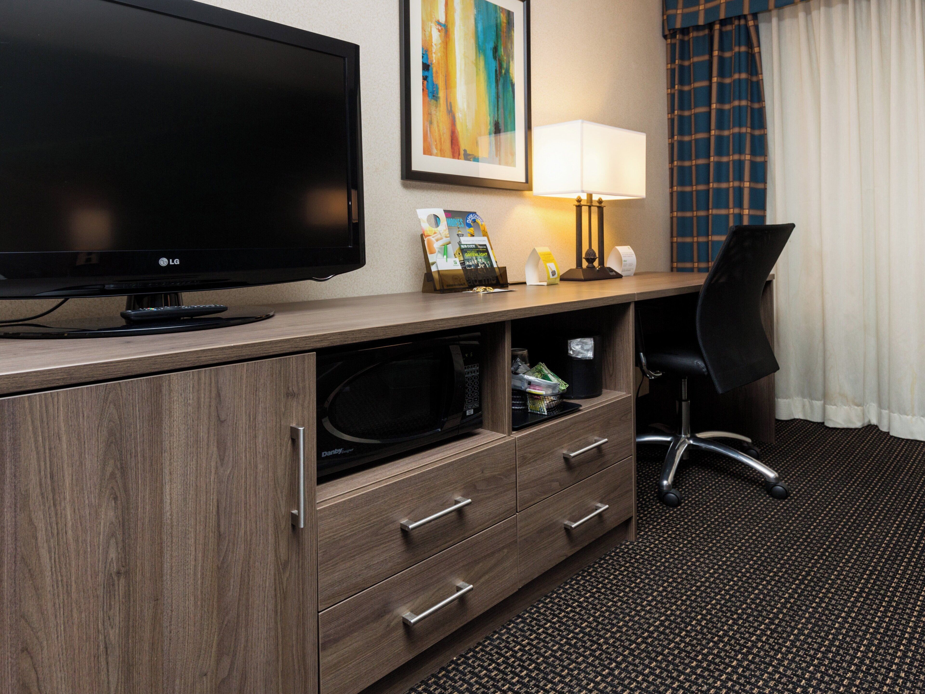 Habitación de hotel con televisión de pantalla plana, escritorio con lámpara, microondas y una silla.