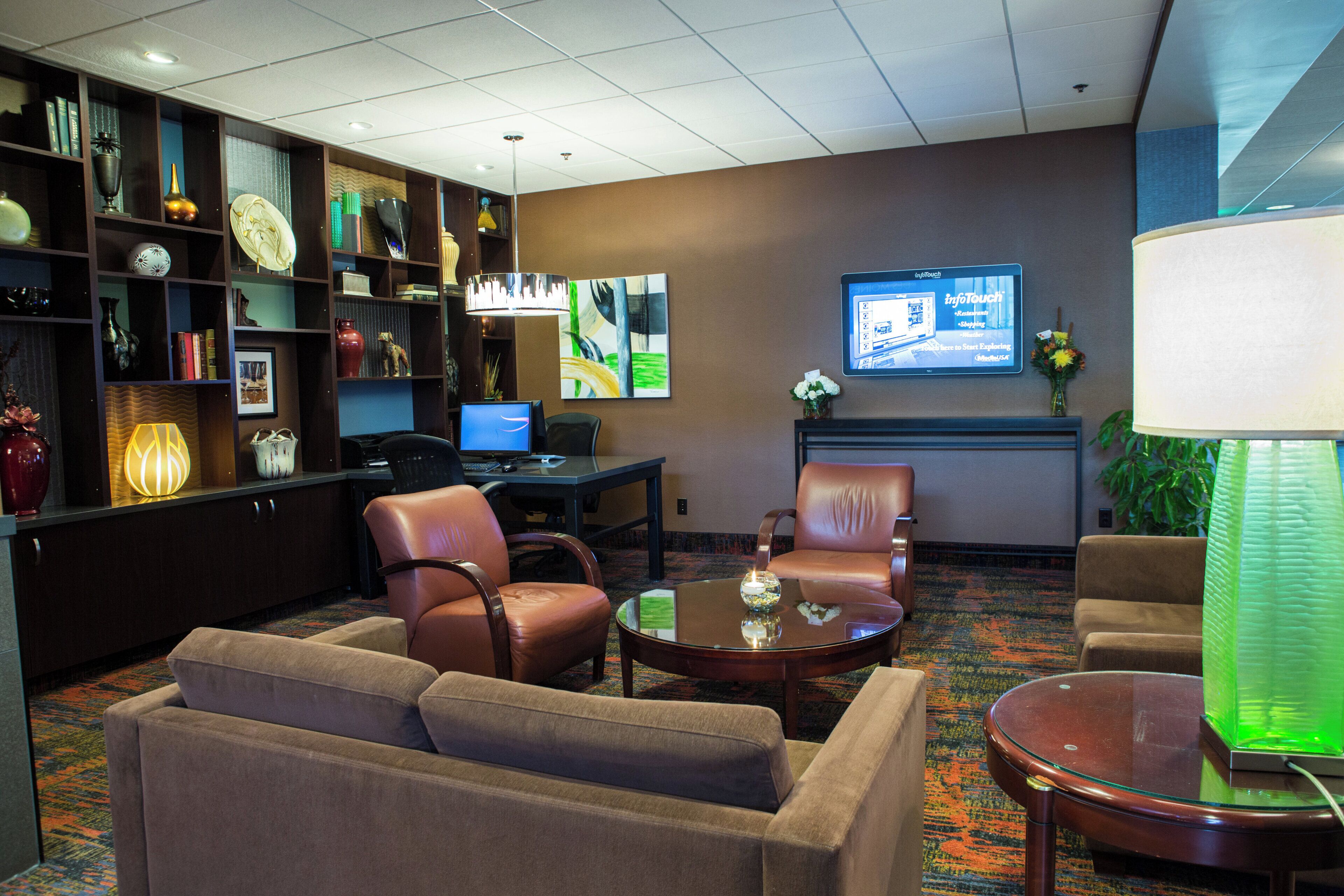 A hotel lobby with a seating area, a desk with a computer, a television, and a bookshelf.