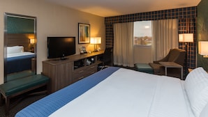 A hotel room with a bed, a desk, a television, a chair, and a window with curtains. - Holiday Inn Downtown - Mercy Area by IHG (Des Moines)