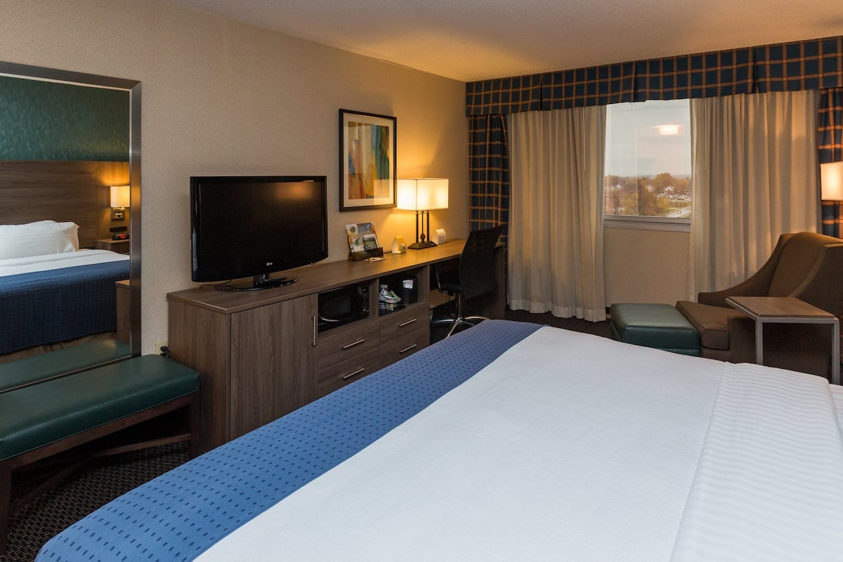 A hotel room with a bed, a desk, a television, a chair, and a window with curtains.