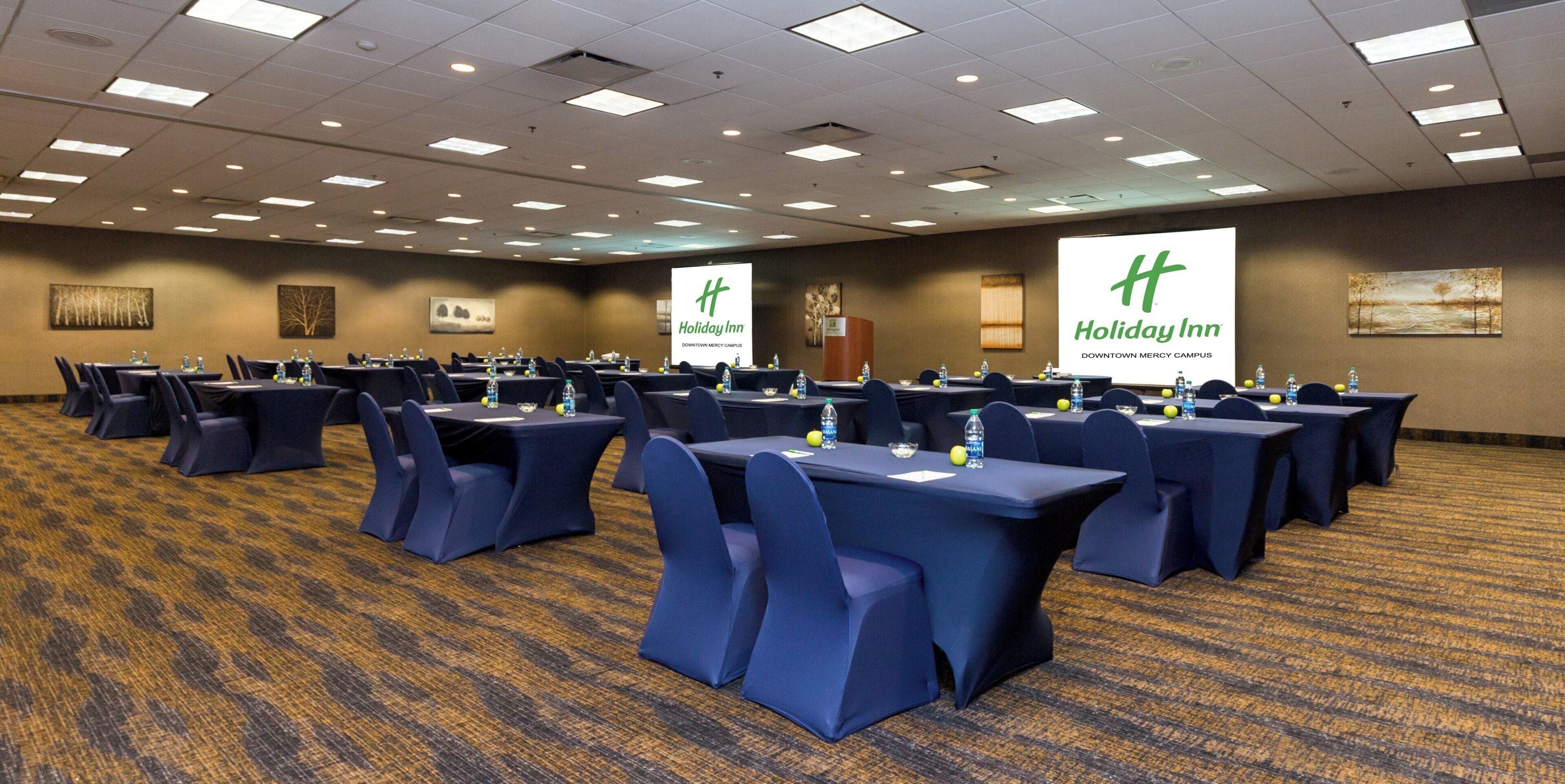 A conference room with tables and chairs, Holiday Inn branding, and a carpeted floor.