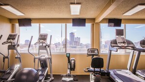 A gym with treadmills, ellipticals, and a stationary bike, with large windows offering a city view. - Holiday Inn Downtown - Mercy Area by IHG (Des Moines)