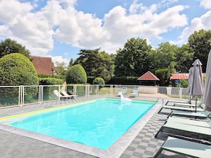 Una piscina rectangular con un flotador inflable de unicornio blanco, rodeada por una cerca blanca, y un pabellón al fondo.