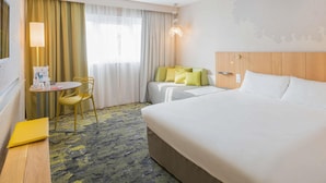 Une chambre d’hôtel avec un grand lit, un bureau avec une chaise, une petite table avec une chaise et une fenêtre avec des rideaux.