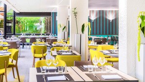 Un restaurante moderno con sillas y mesas amarillas, ventanas amplias que ofrecen vistas a zonas verdes y una combinación de mesas dentro y fuera.