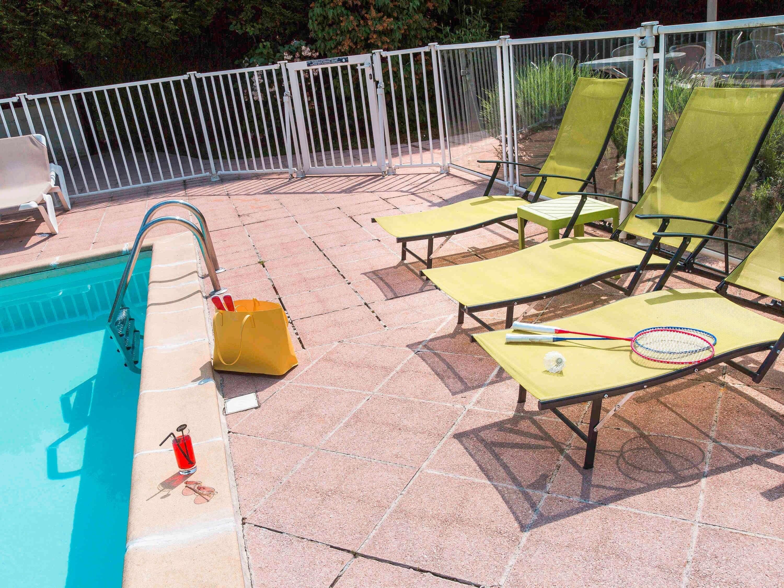 A poolside area with a pool, lounge chairs, a yellow bag, and a badminton racket.
