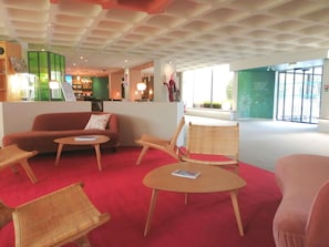 A lobby with a red carpet, a sofa, wicker chairs, a small table, and a bar area in the background.