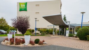 Una entrada de hotel moderna con un llamativo letrero verde, un corredor cubierto y zonas ajardinadas.
