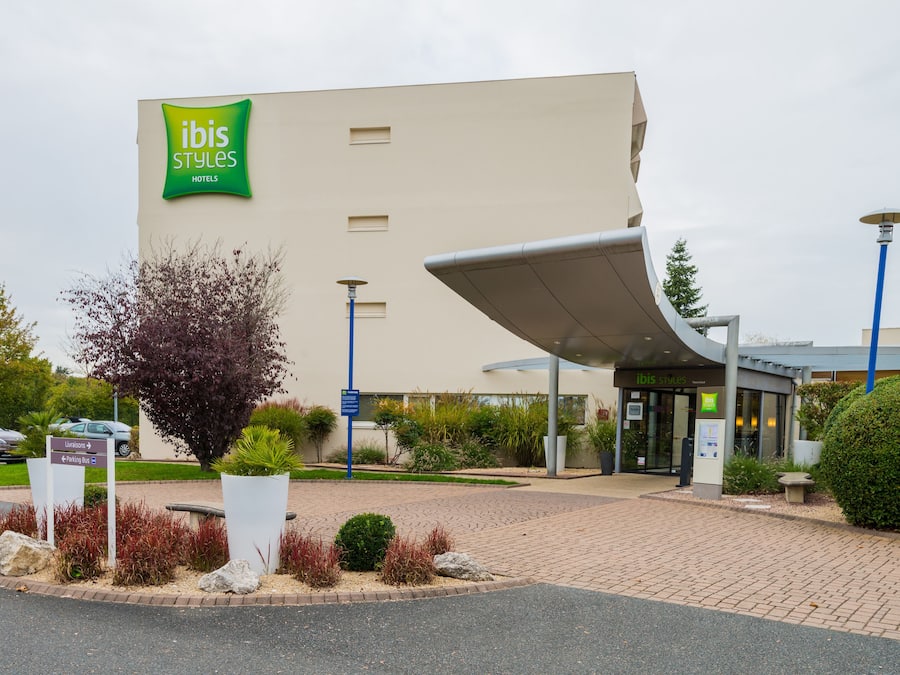 Una entrada de hotel moderna con un llamativo letrero verde, un corredor cubierto y zonas ajardinadas.