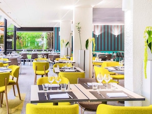 Un restaurante moderno con sillas y mesas amarillas, ventanas amplias que ofrecen vistas a zonas verdes y una combinación de mesas dentro y fuera.