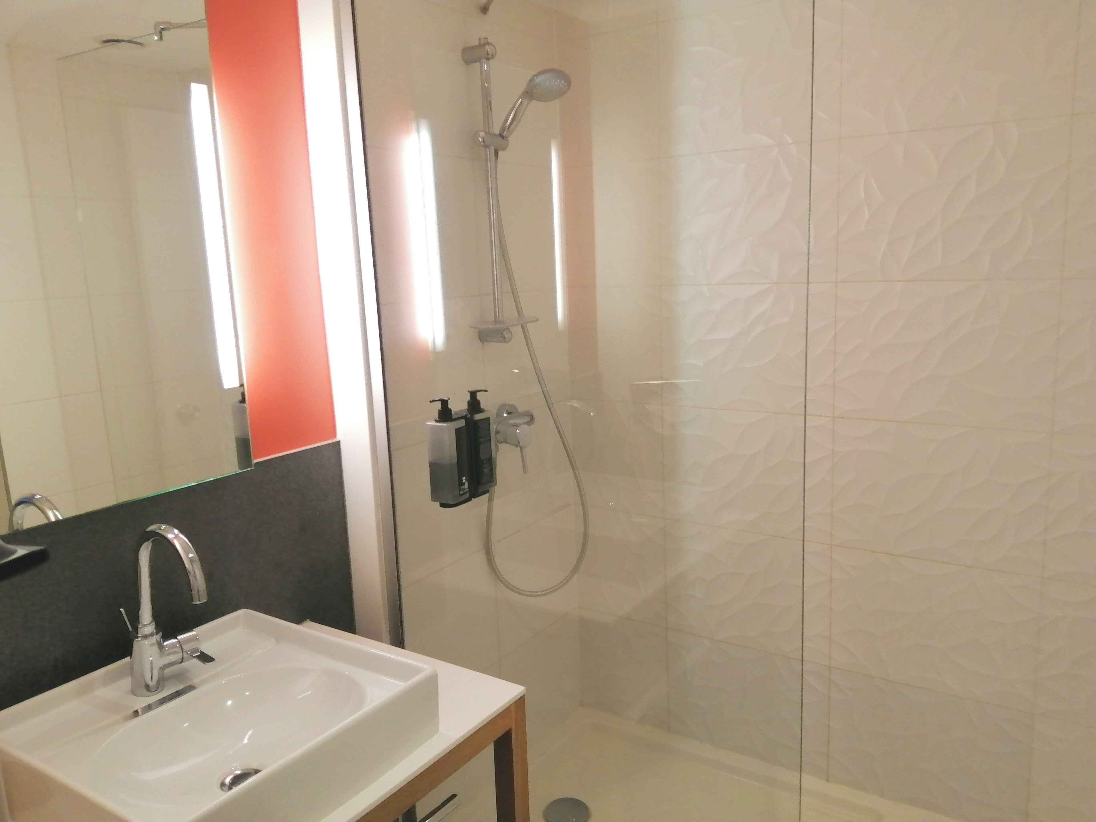 Un baño con lavamanos, espejo, ducha y artículos de aseo.