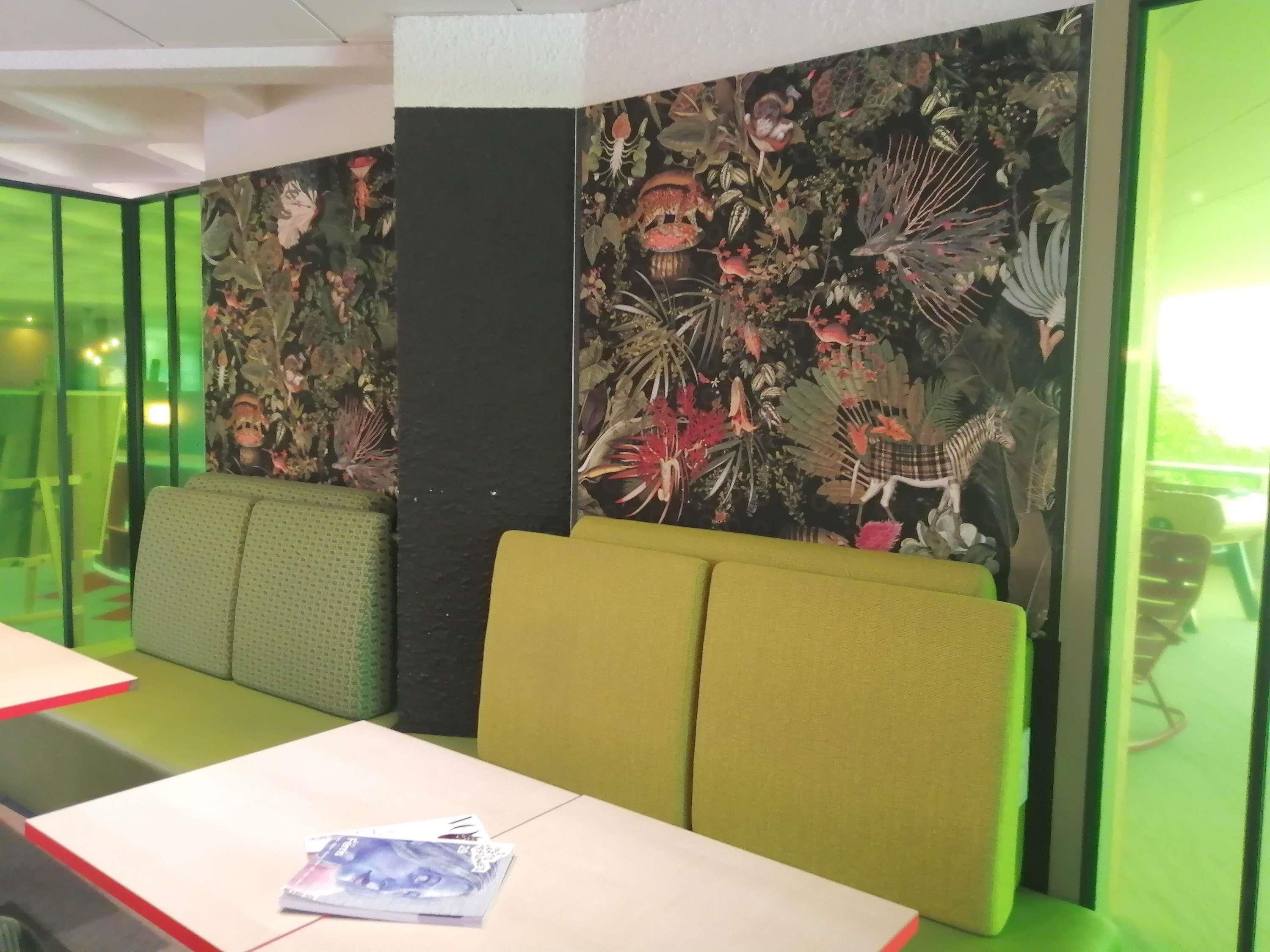 A restaurant interior with green booths, a high ceiling, and a wall with a floral mural.