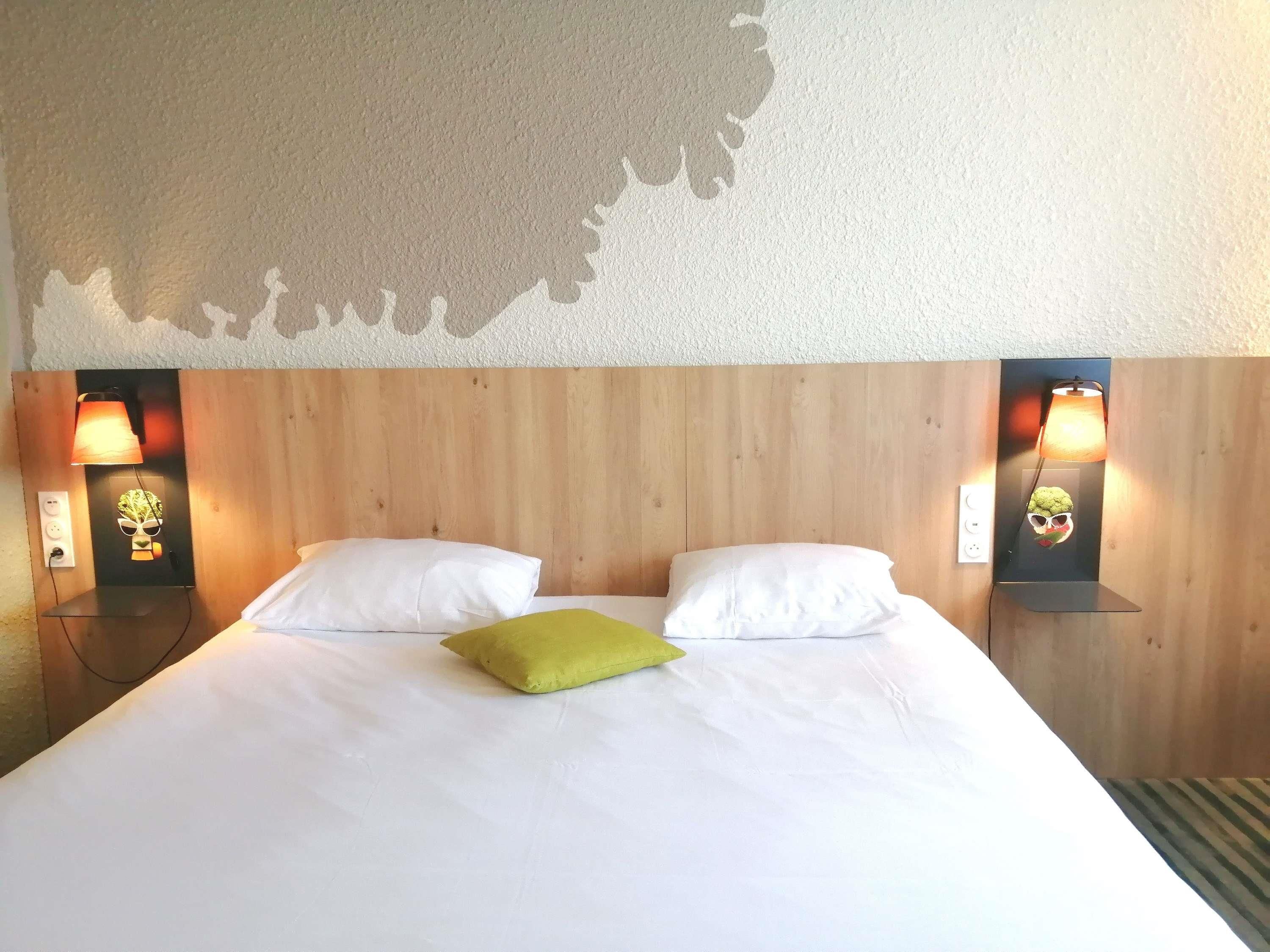 A hotel room with a wooden headboard, two bedside lamps, white bedding, and a green pillow.
