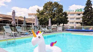 Una piscina con un flotador de unicornio, sillas de descanso, sombrillas y un edificio con un letrero.
