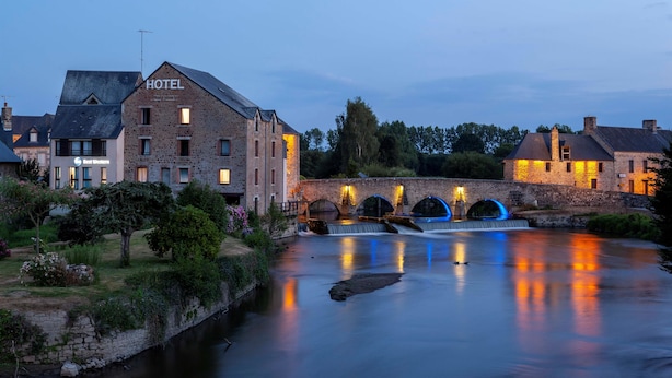 A hotel with a brick facade, a bridge with arches, and a calm river reflecting lights. - Best Western Le Moulin De Ducey (Ducey-les-Chéris)
