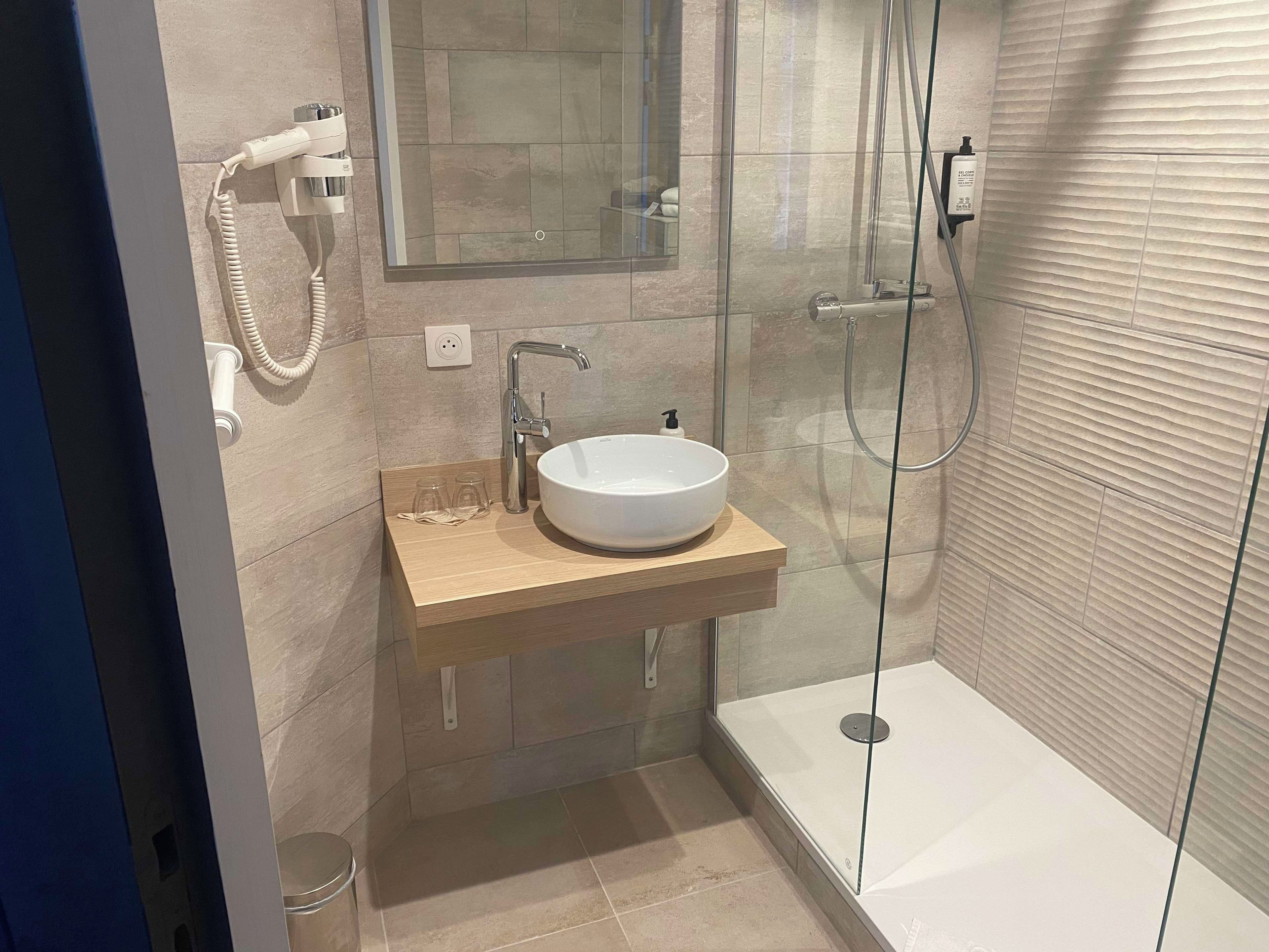Ein modernes Badezimmer mit einer Duschkabine, einem weißen Waschbecken und einem Handtuchspender.