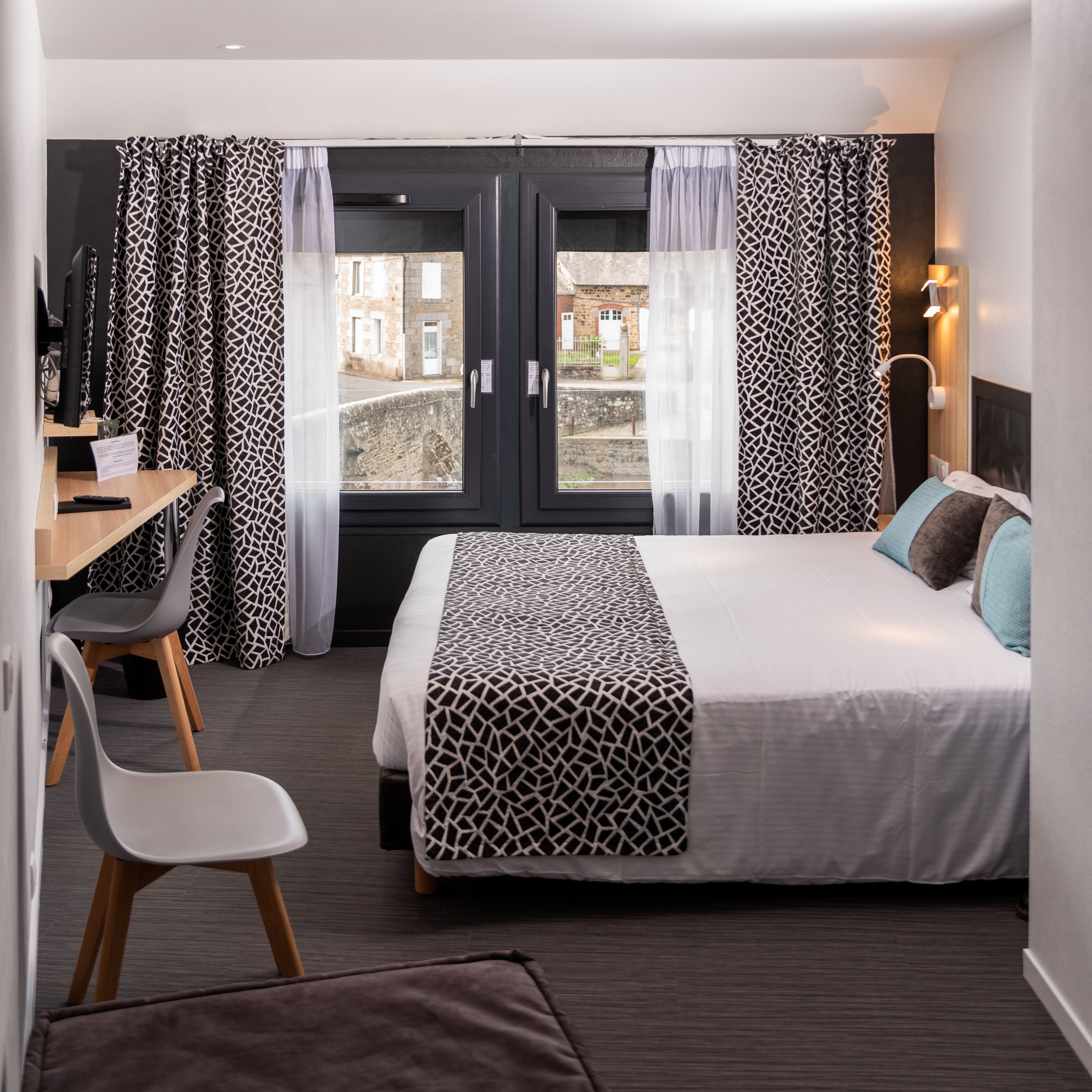 A hotel room with a bed, a desk, a chair, and a view of the outside.