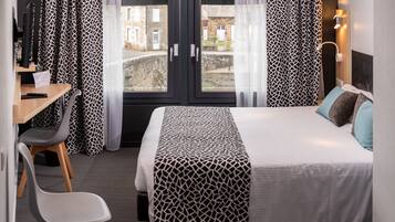 A hotel room with a bed, a desk, a chair, and a view of the outside.