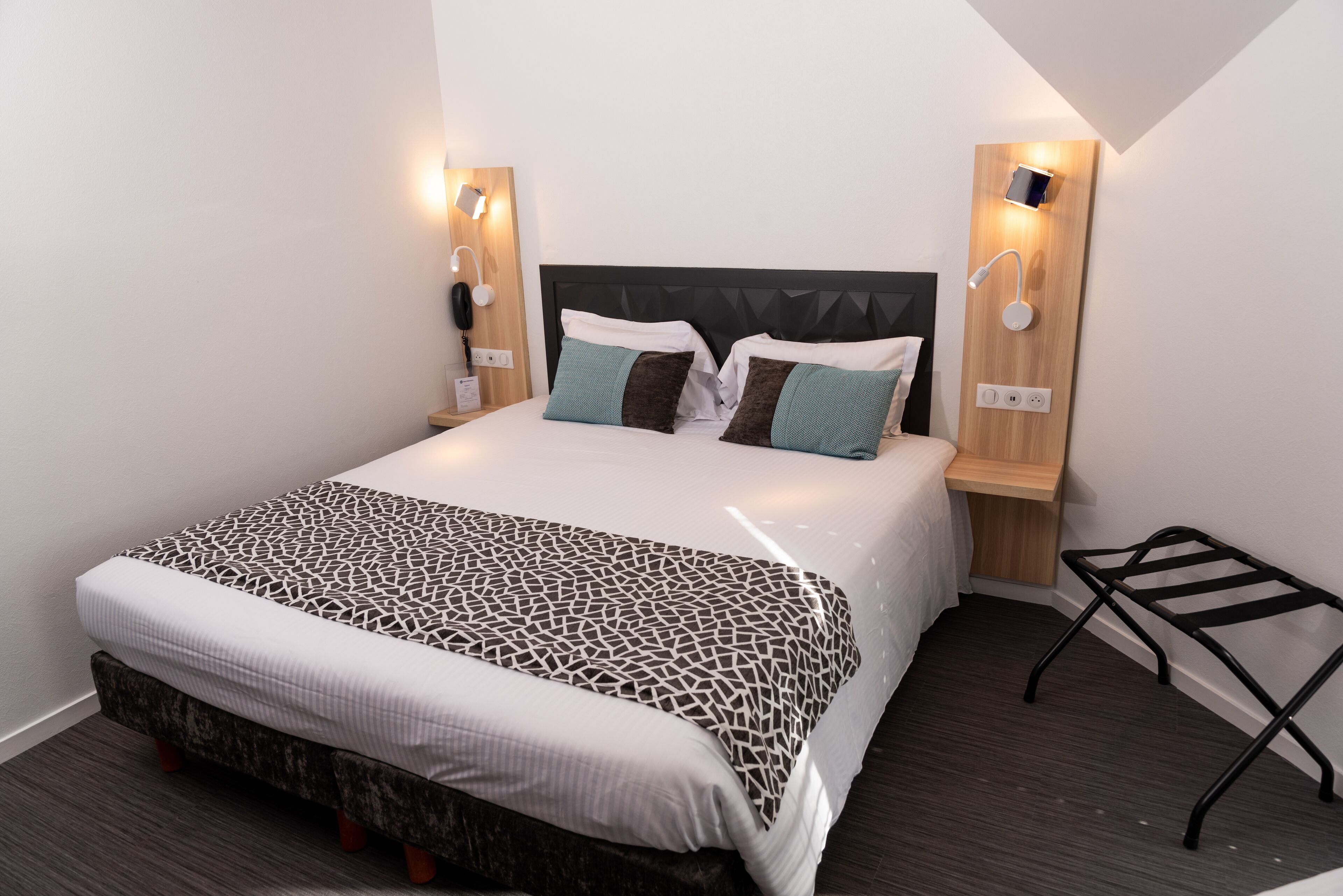 A neatly made bed with a geometric patterned bedspread, two pillows, and a bedside table with a lamp.