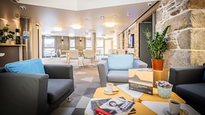 A modern lobby with grey sofas, a coffee table, and a bookshelf. - Best Western Le Moulin De Ducey (Ducey-les-Chéris)