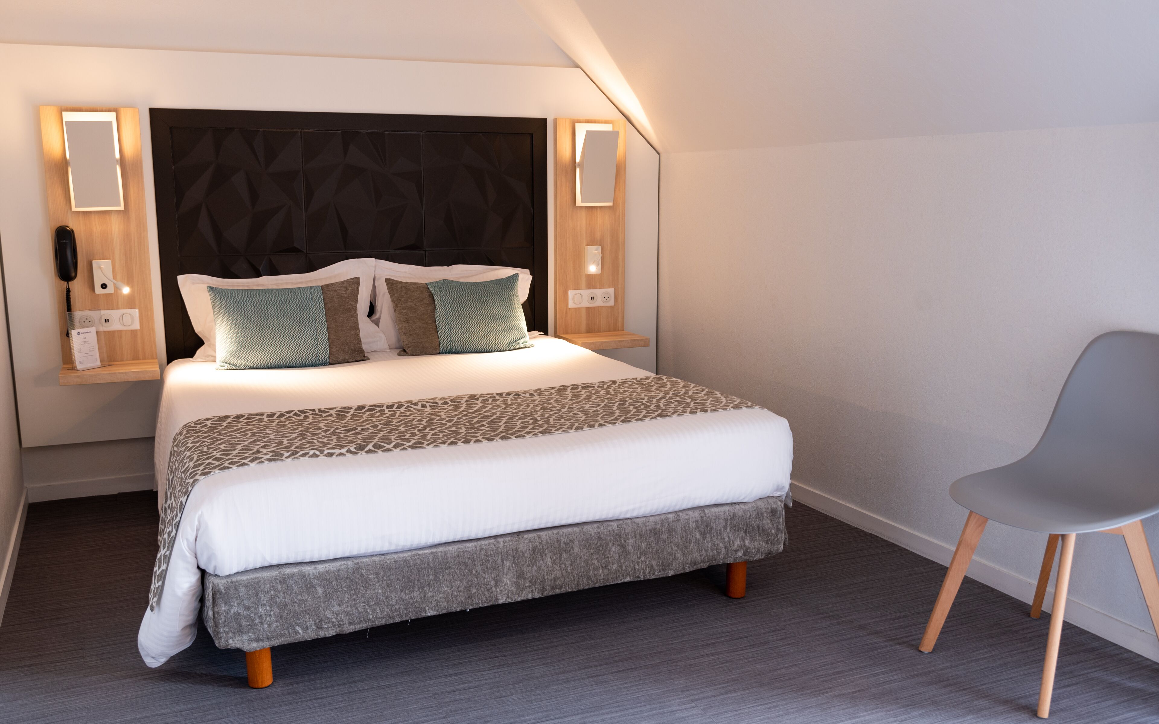 A neatly made bed with a patterned bedspread, two pillows, and a bedside table with a lamp.