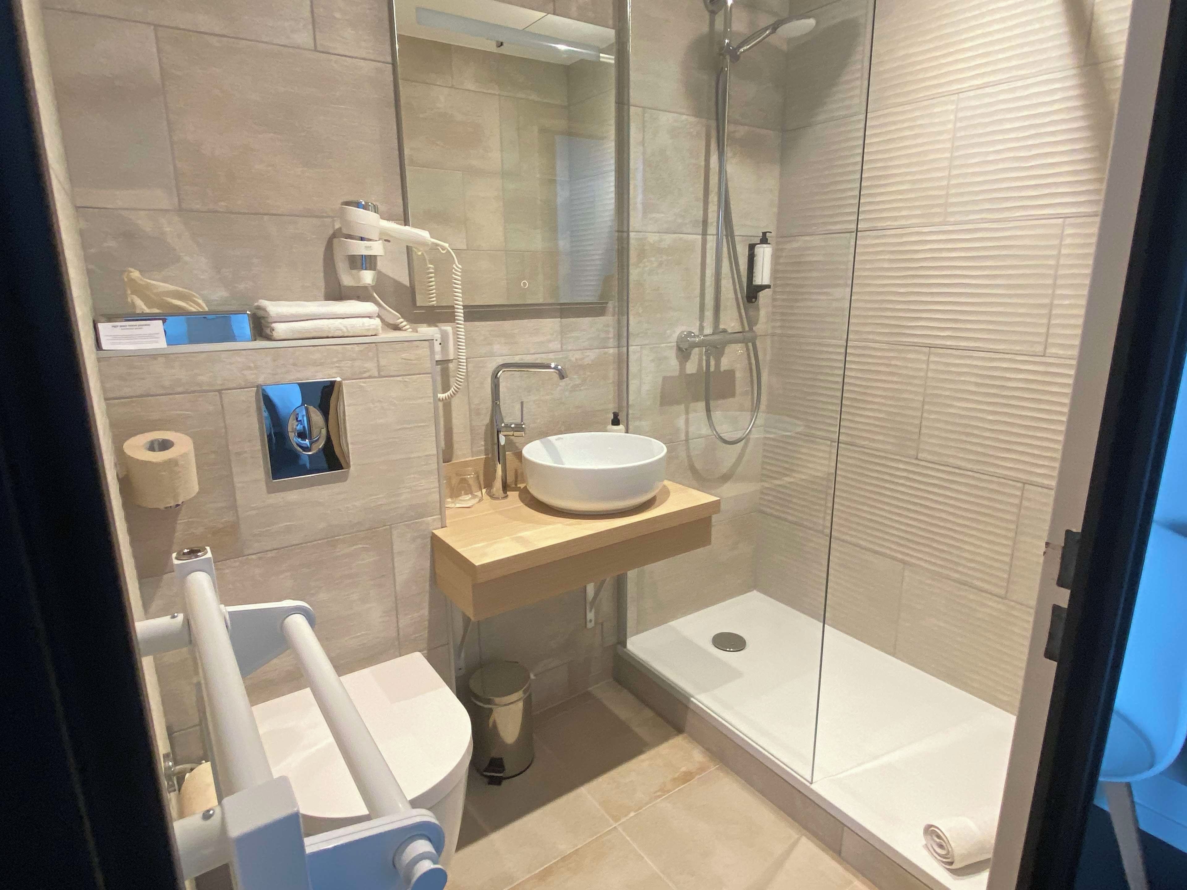 Un bany modern amb un lavabo blanc, un vàter portàtil, un vàter i una dutxa amb portes de vidre.