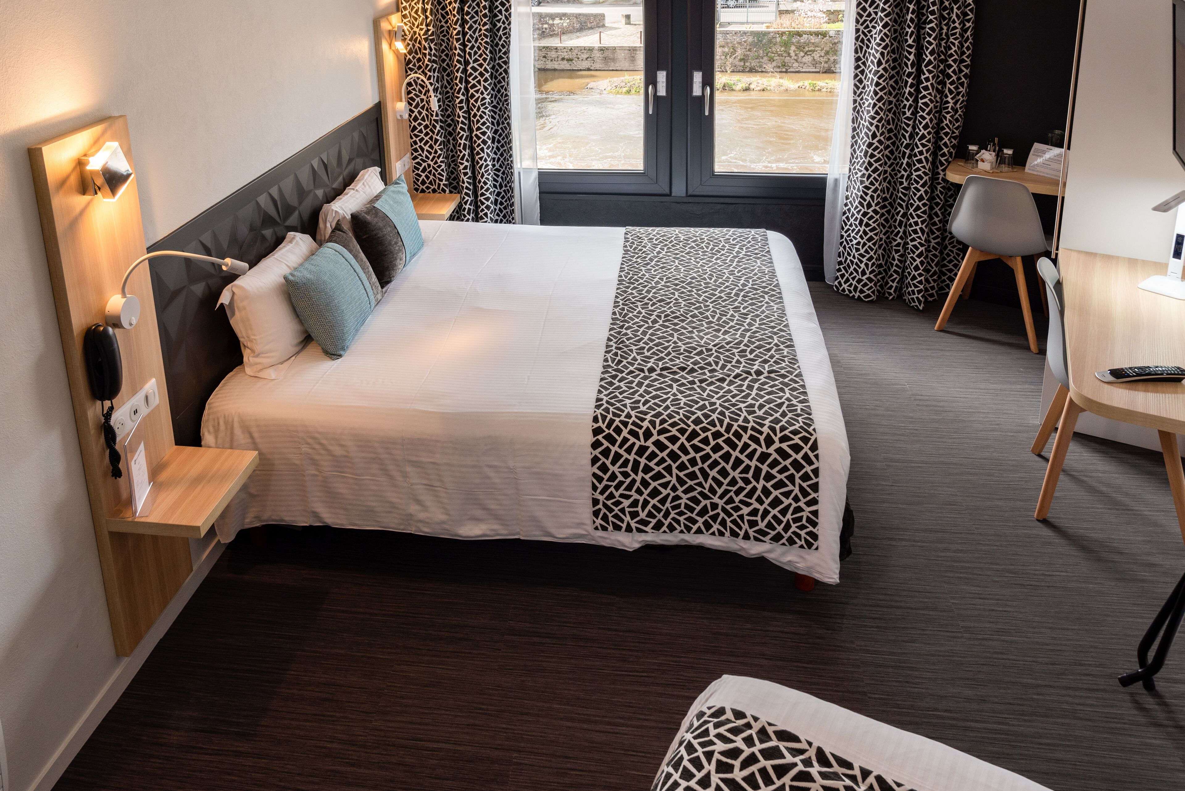 Una habitación de hotel con cama, mesita de noche, lámpara y escritorio con silla.
