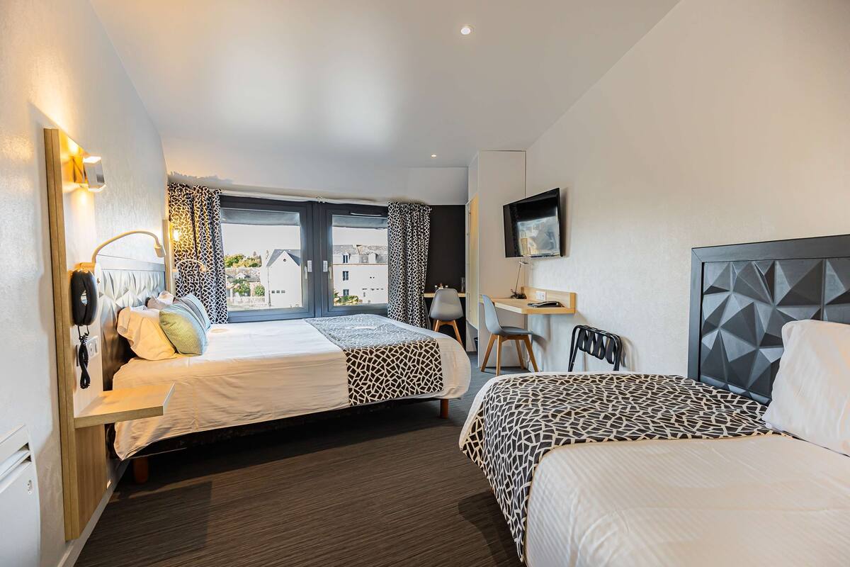 A hotel room with two beds, a desk, a chair, and a TV.