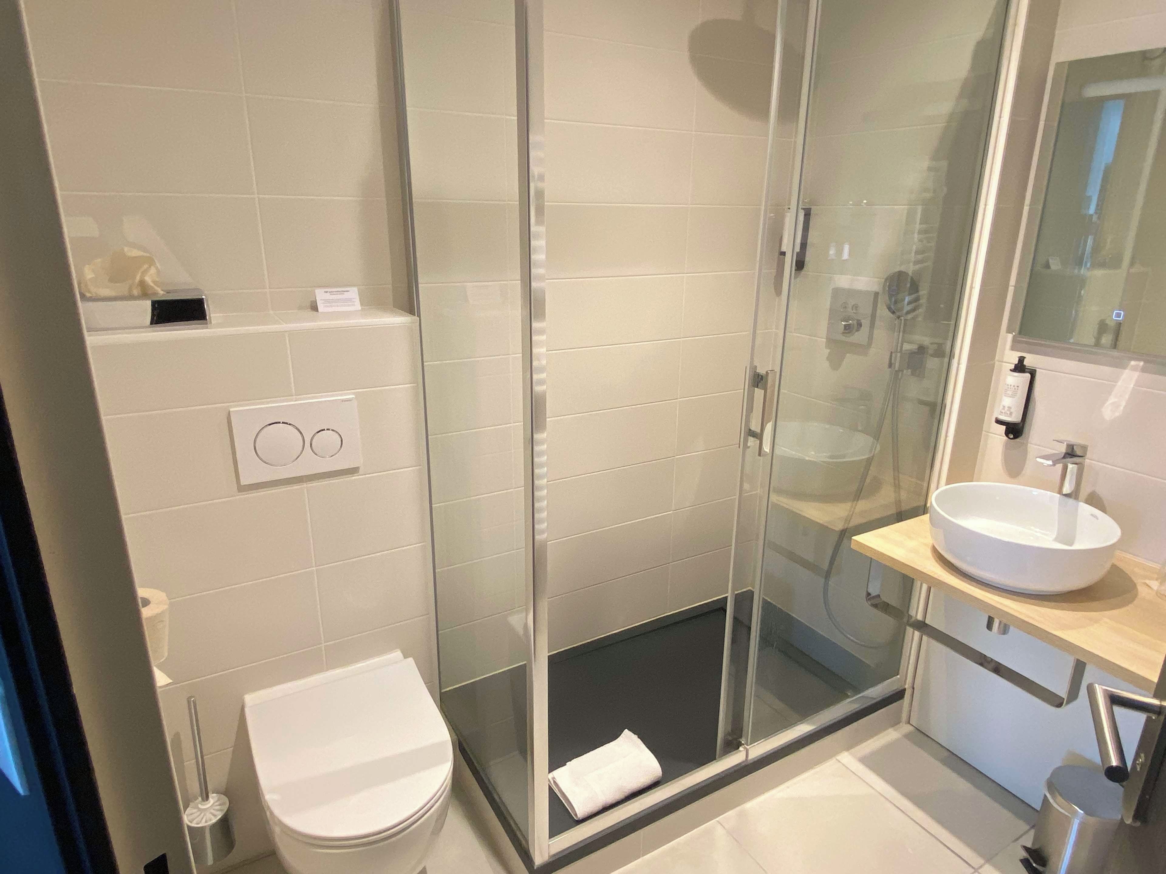 A modern bathroom with a glass-enclosed shower, a white toilet, and a sink with a mirror above it.