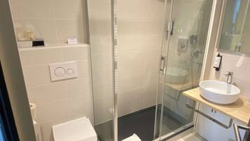 Ein modernes Badezimmer mit einer gläsernen Duschkabine, einer weißen Toilette und einem Waschbecken mit Spiegel darüber.