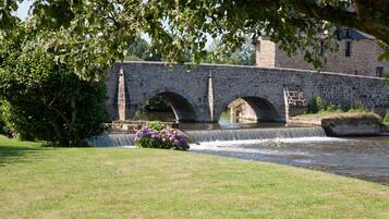 A stone bridge over a river with a grassy foreground and a building in the background.