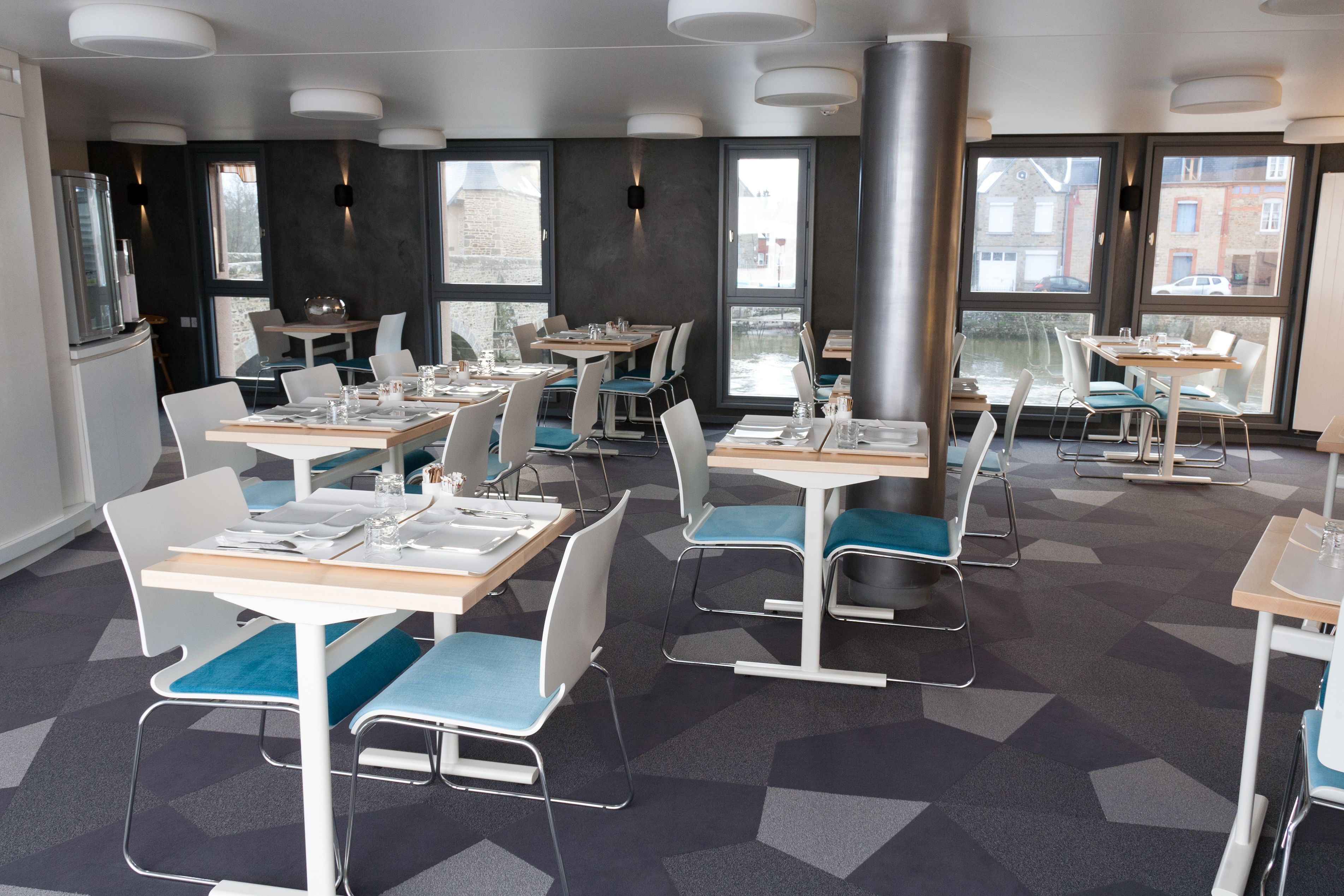 A modern dining area with tables and chairs, large windows, and a geometric carpet pattern.