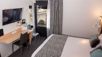 Quarto de hotel com cama, secretária e cadeira, televisão e janela com cortinas.