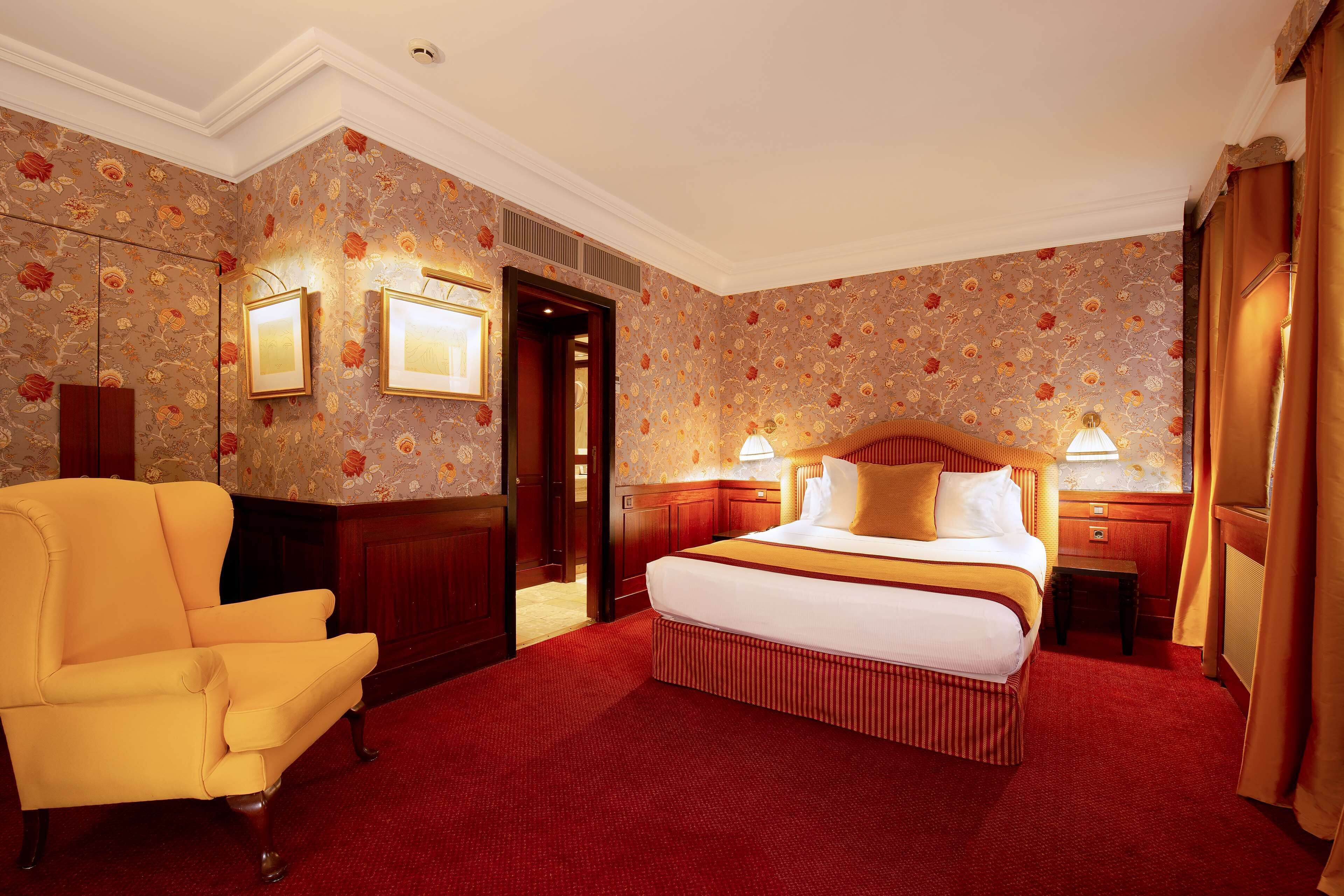 Ein Hotelzimmer mit einem großen Bett, einem gelben Sessel und blumigem Wandpapier.