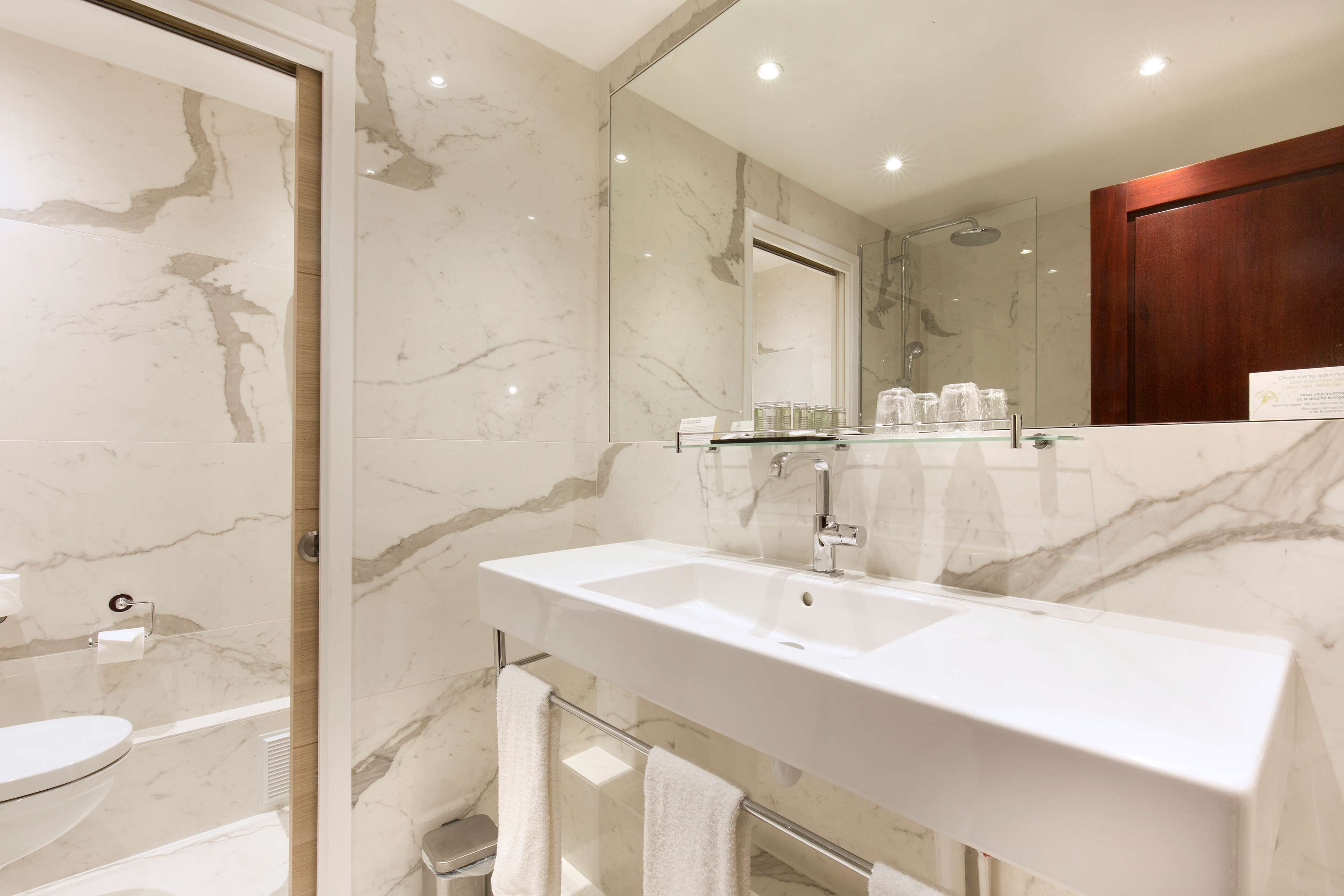 A modern bathroom with a marble sink, a glass shower enclosure, and a large mirror.