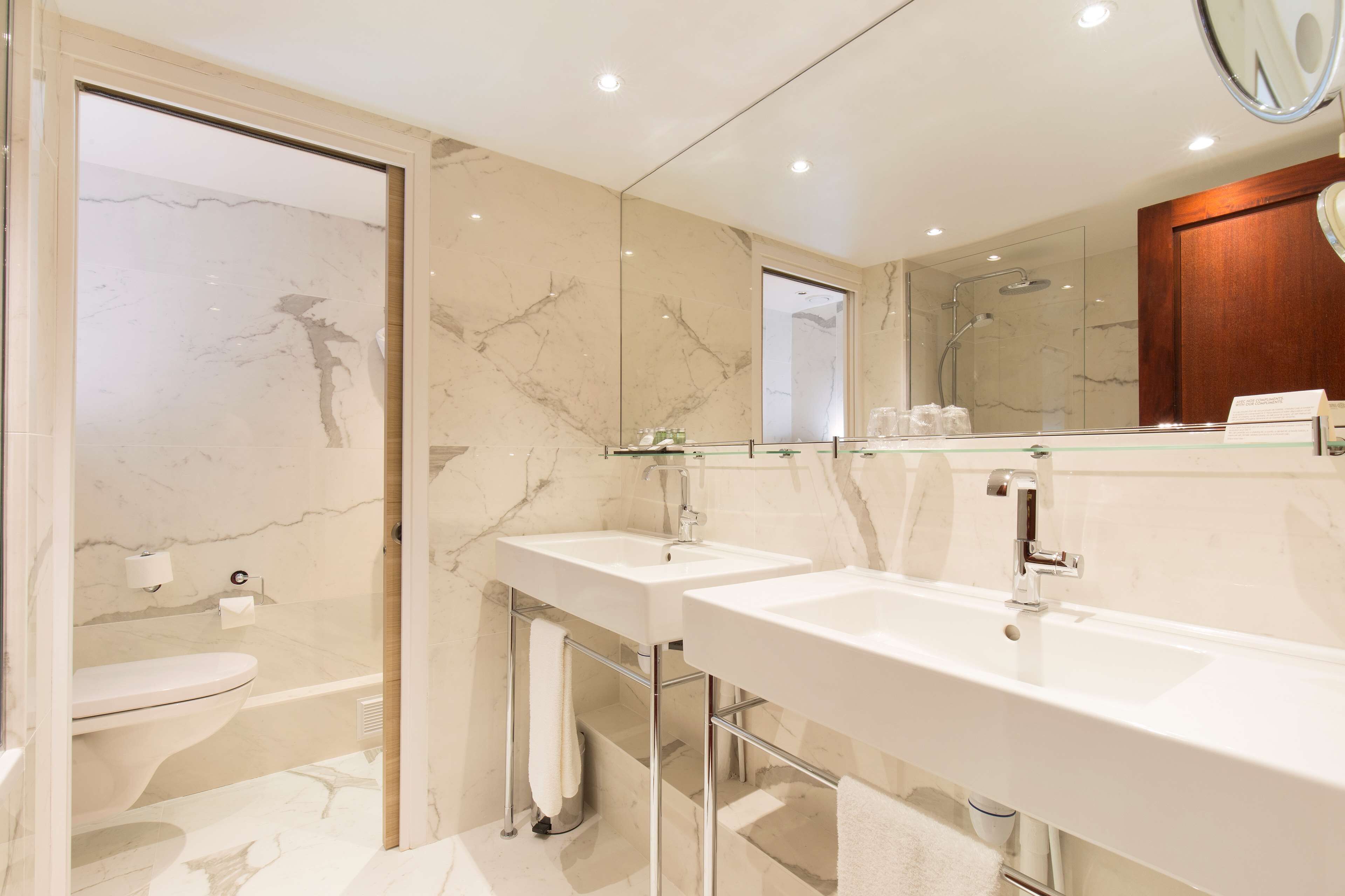 A modern bathroom with two sinks, a toilet, and a shower.