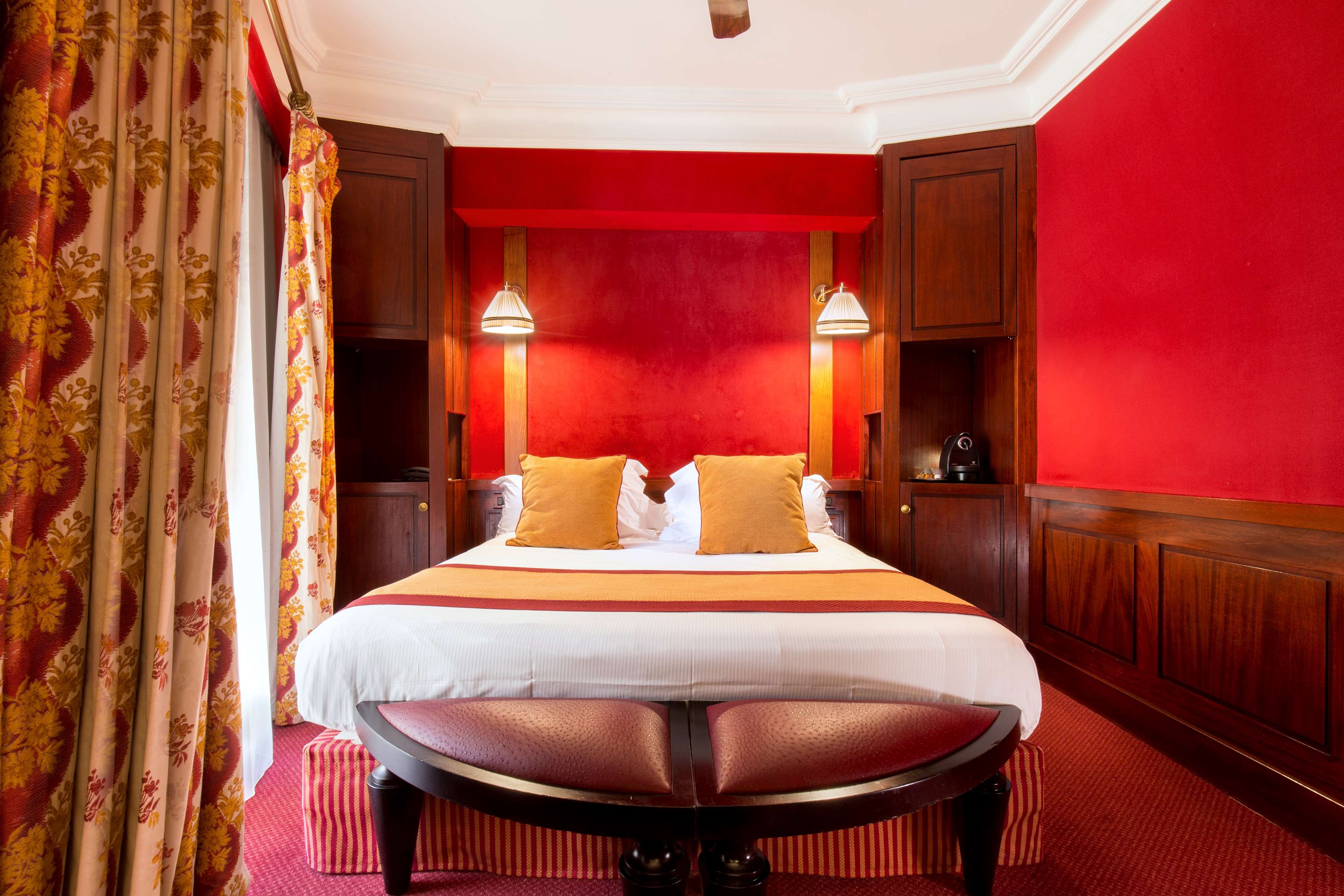 A hotel room with a large bed, two bedside lamps, a wooden nightstand, and a red carpet.