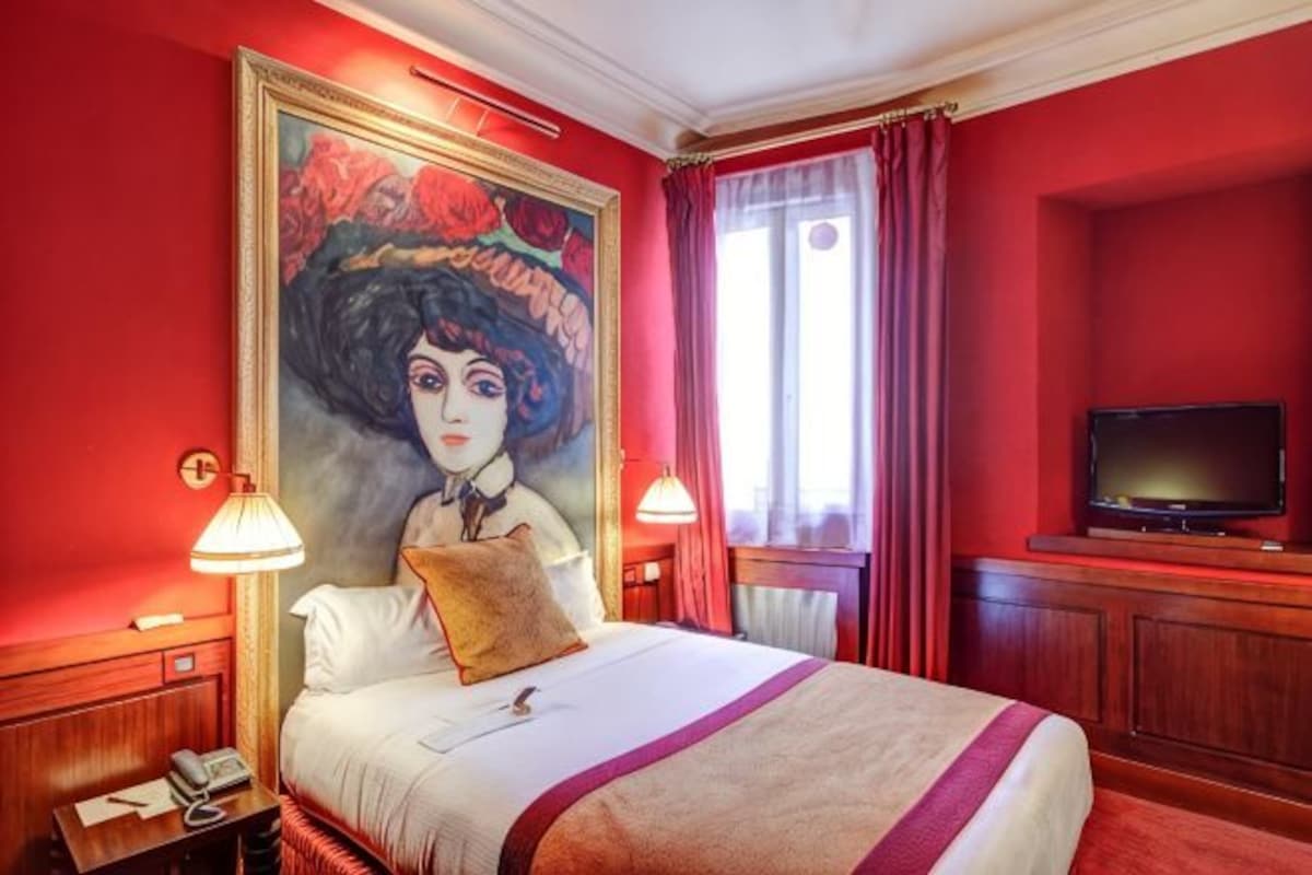 A hotel room with a large painting on the wall, a bed with a red-striped blanket, a television on a wooden cabinet, and a window with red curtains.