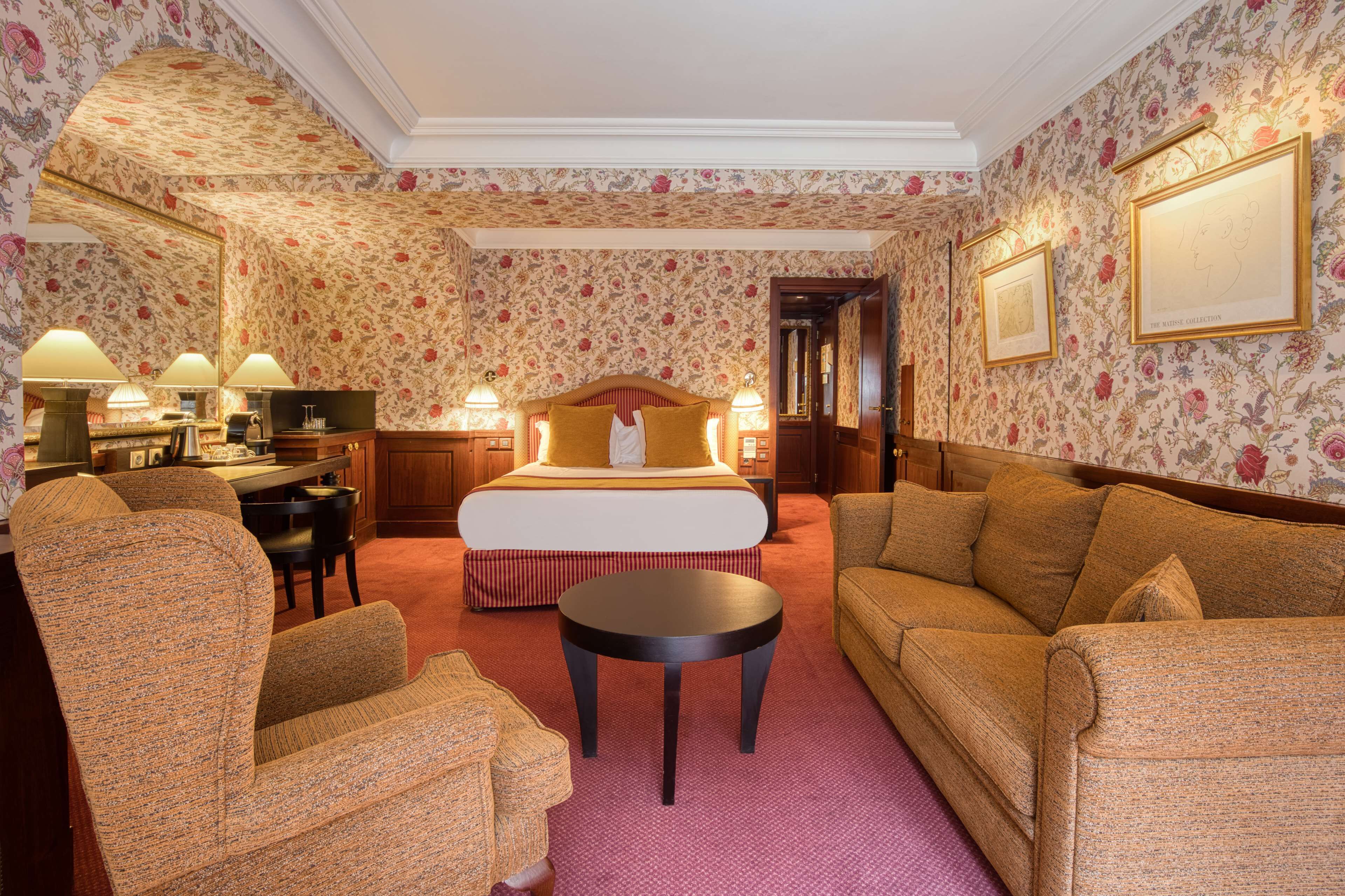 A hotel room with a bed, two armchairs, a sofa, a small table, and a desk with lamps.