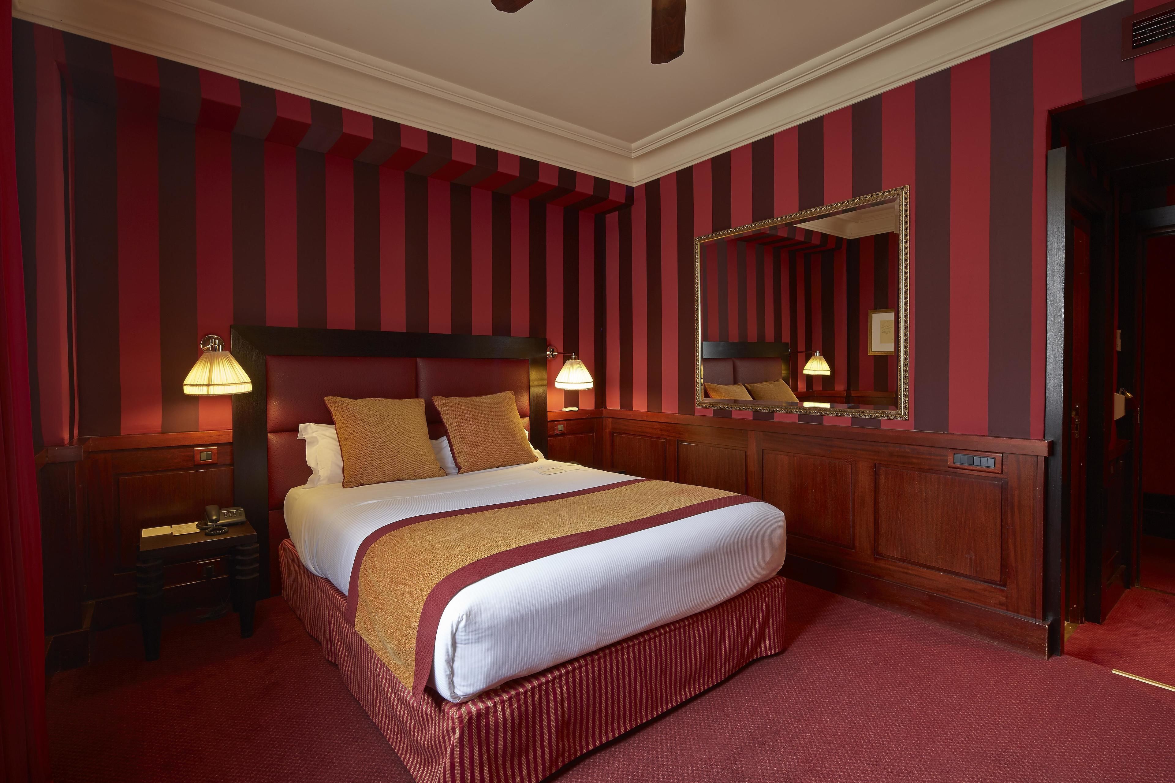 A hotel room with a large bed, two bedside tables, a mirror, and striped wallpaper.