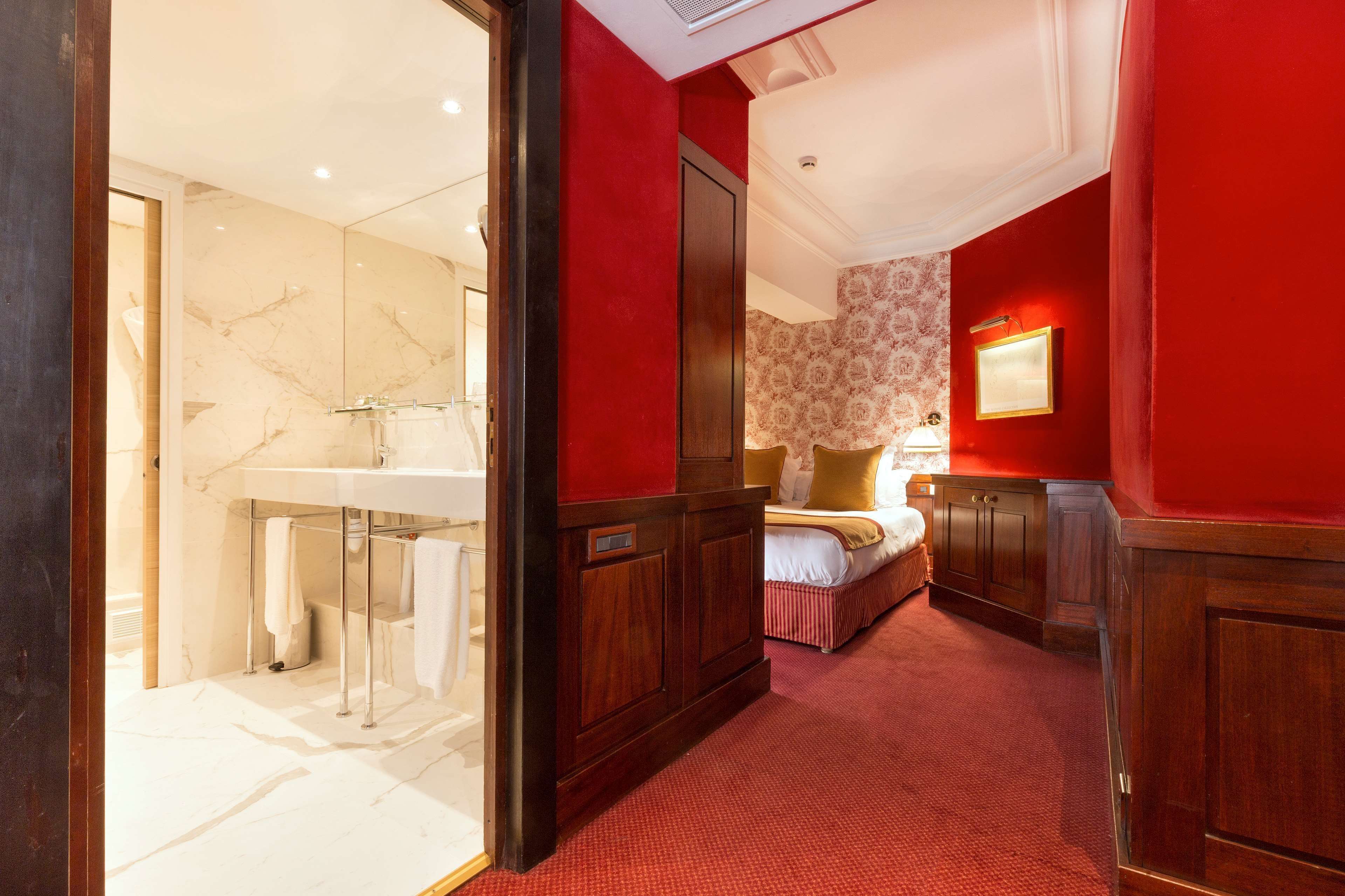 A hotel room with a bathroom, a bed, and a red carpeted hallway.