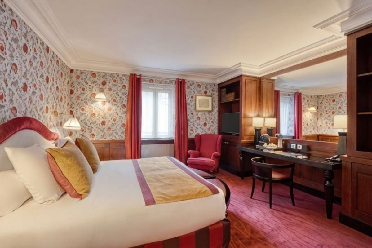 A hotel room with a bed, desk, chairs, and a television.