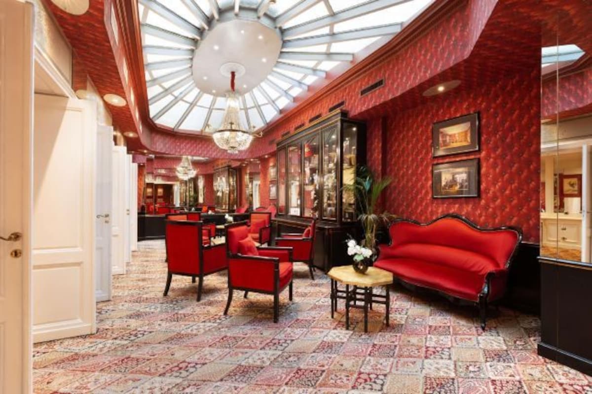 A lobby with red upholstered seating, a patterned carpet, and a glass ceiling.