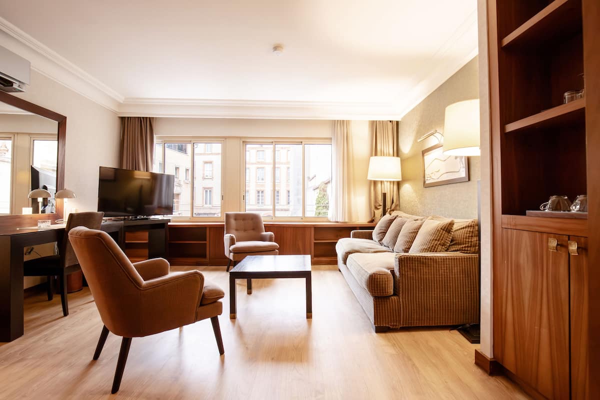 Una sala de estar bien iluminada con un sofá, sillones, una mesa de centro, un televisor y un ventanal con cortinas.